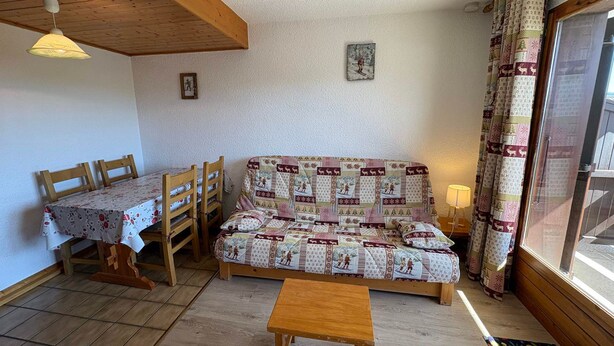 A cozy room with a wooden ceiling, a sofa with a patterned cover, a dining table with chairs, and a window with curtains. - Les Saisies - Studio Cabin 4 People, South (Les Saisies)