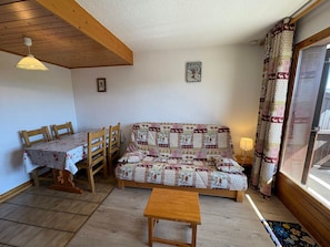 Una habitación acogedora con techo de madera, un sofá con funda estampada, una mesa de comedor con sillas y una ventana con cortinas.