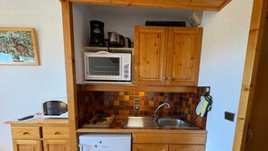 A compact kitchen with wooden cabinets, a microwave, a sink, and a refrigerator.