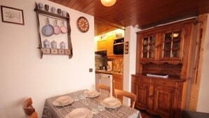 Un coin repas avec une table dressée pour quatre personnes, des meubles en bois et une cuisine en arrière-plan.