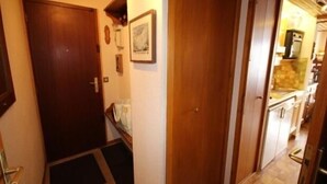Un couloir étroit avec des portes en bois, un petit tapis et une cuisine visible au fond.