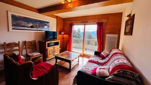 Una sala de estar acogedora con televisión, muebles de madera, un sofá y vistas a montañas a través de un ventanal amplio.
