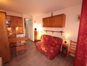 Een gezellige woonkamer met een houten bank, een eettafel en een keuken op de achtergrond.