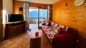 A cozy living room with a wooden interior, a television on a wooden cabinet, a red sofa, and a large clock on the wall.