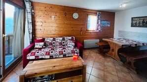 A cozy room with wooden walls, a red sofa, a wooden table, and a window with curtains.