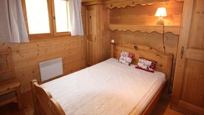 A wooden room with a bed, a nightstand, a lamp, and a window with curtains.