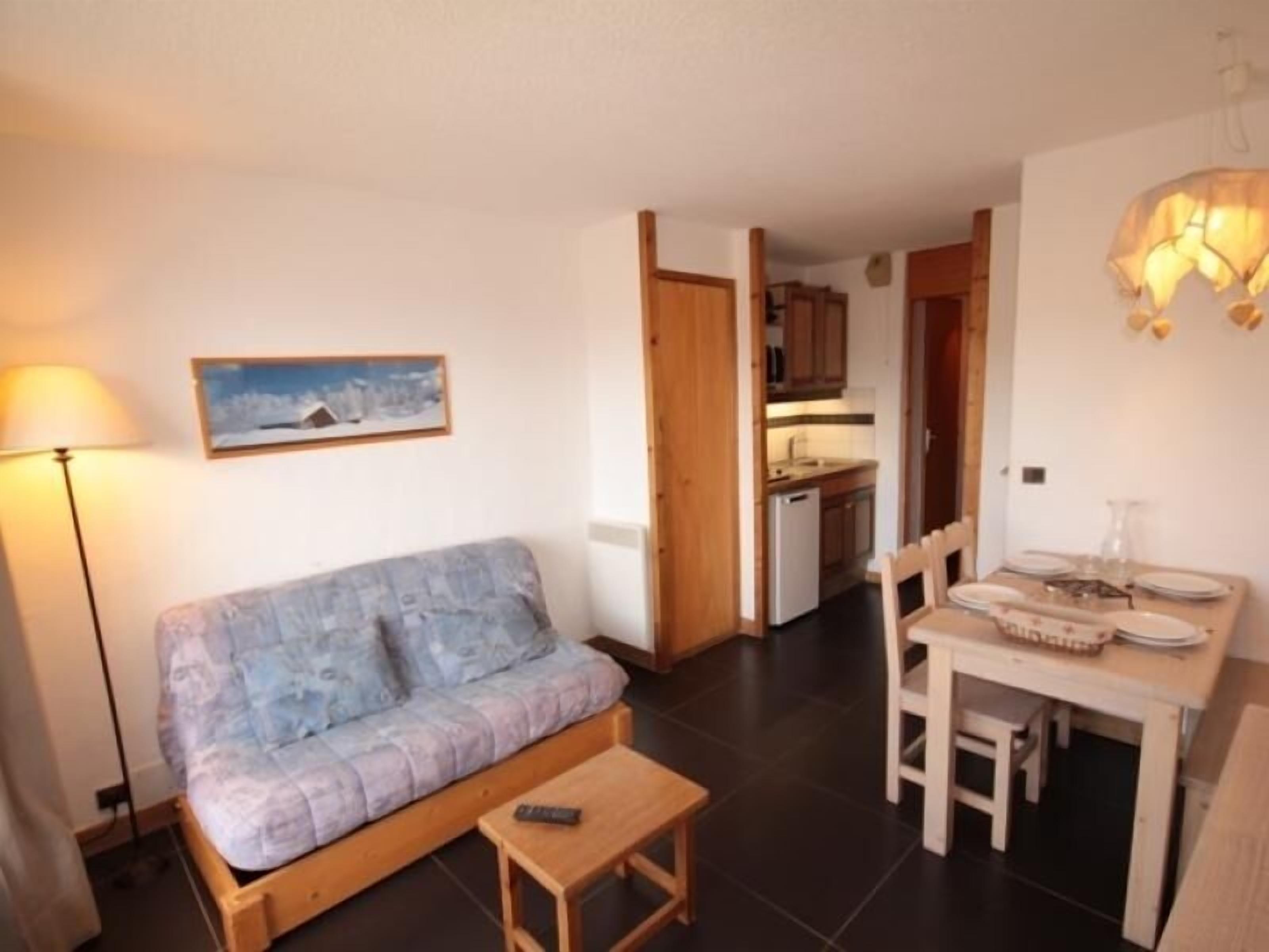 Un espace de vie compact comprenant un canapé, une petite table, une table à manger avec des chaises, un coin cuisine et une lampe.