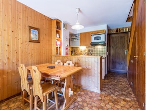 Un interior de madera con una mesa y sillas para comer, una zona de cocina con armarios y electrodomésticos, y piso de baldosas.