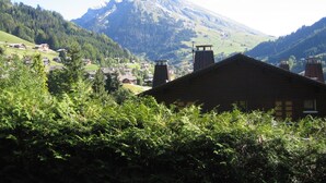 Een bergdorpslandschap met traditionele houten huizen, een opvallende bergtop in de verte en glooiende groene heuvels.
