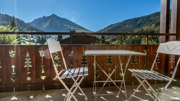 Een balkon met een tafel en stoelen, met uitzicht op een bergachtig landschap.