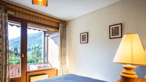 Een slaapkamer met een bed, een raam met gordijnen, een lamp en twee ingelijste foto's aan de muur.