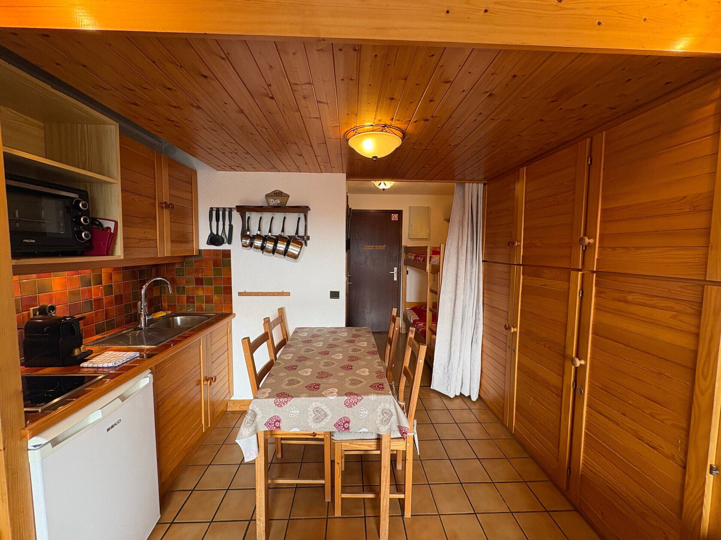 A compact kitchen with wooden cabinets, a microwave, a sink, and a dining table with chairs.
