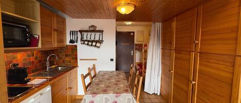 A compact kitchen with wooden cabinets, a microwave, a sink, and a dining table with chairs.