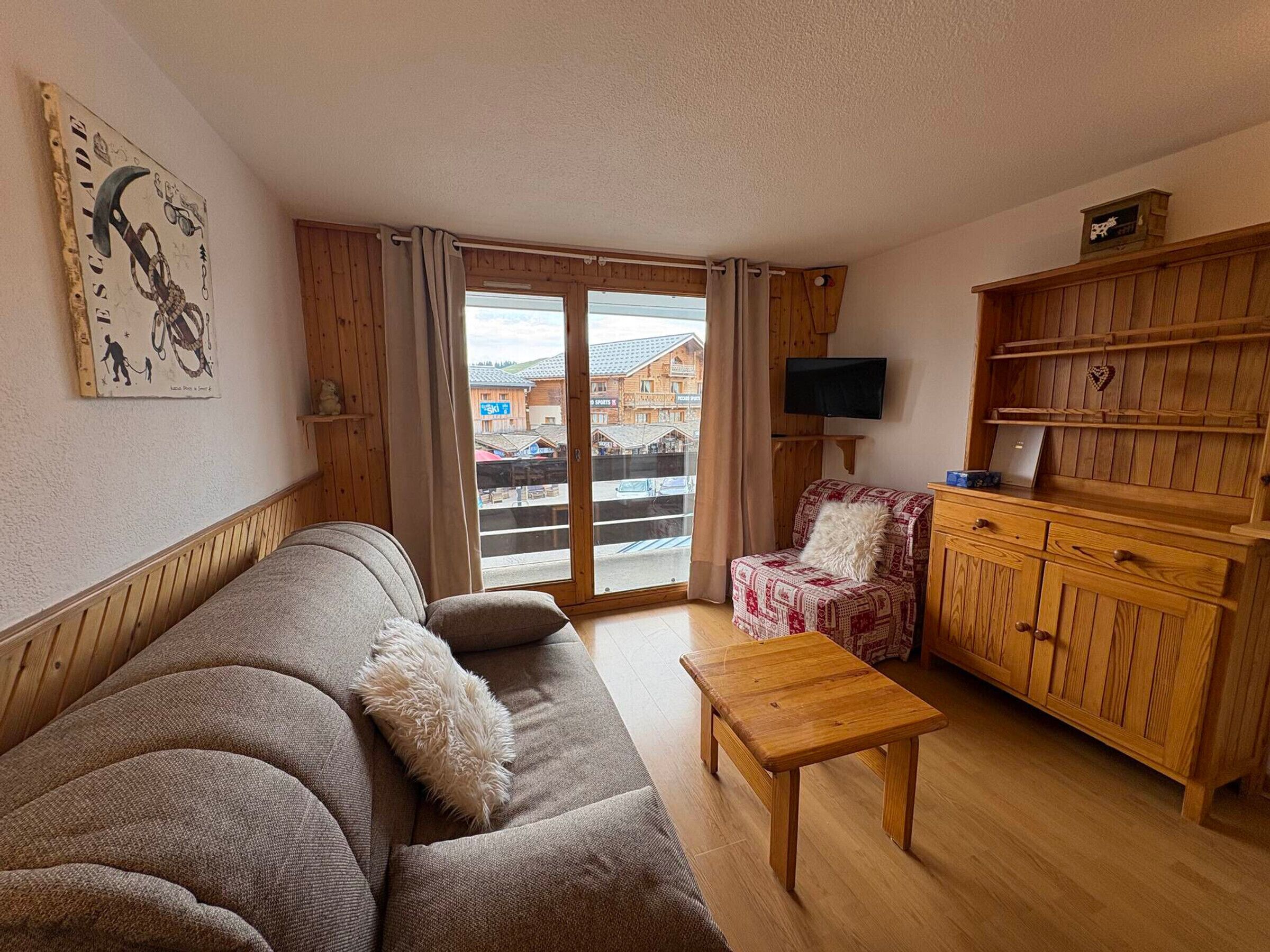 A living room with a sofa, a wooden cabinet, a television, and a view of a ski resort.