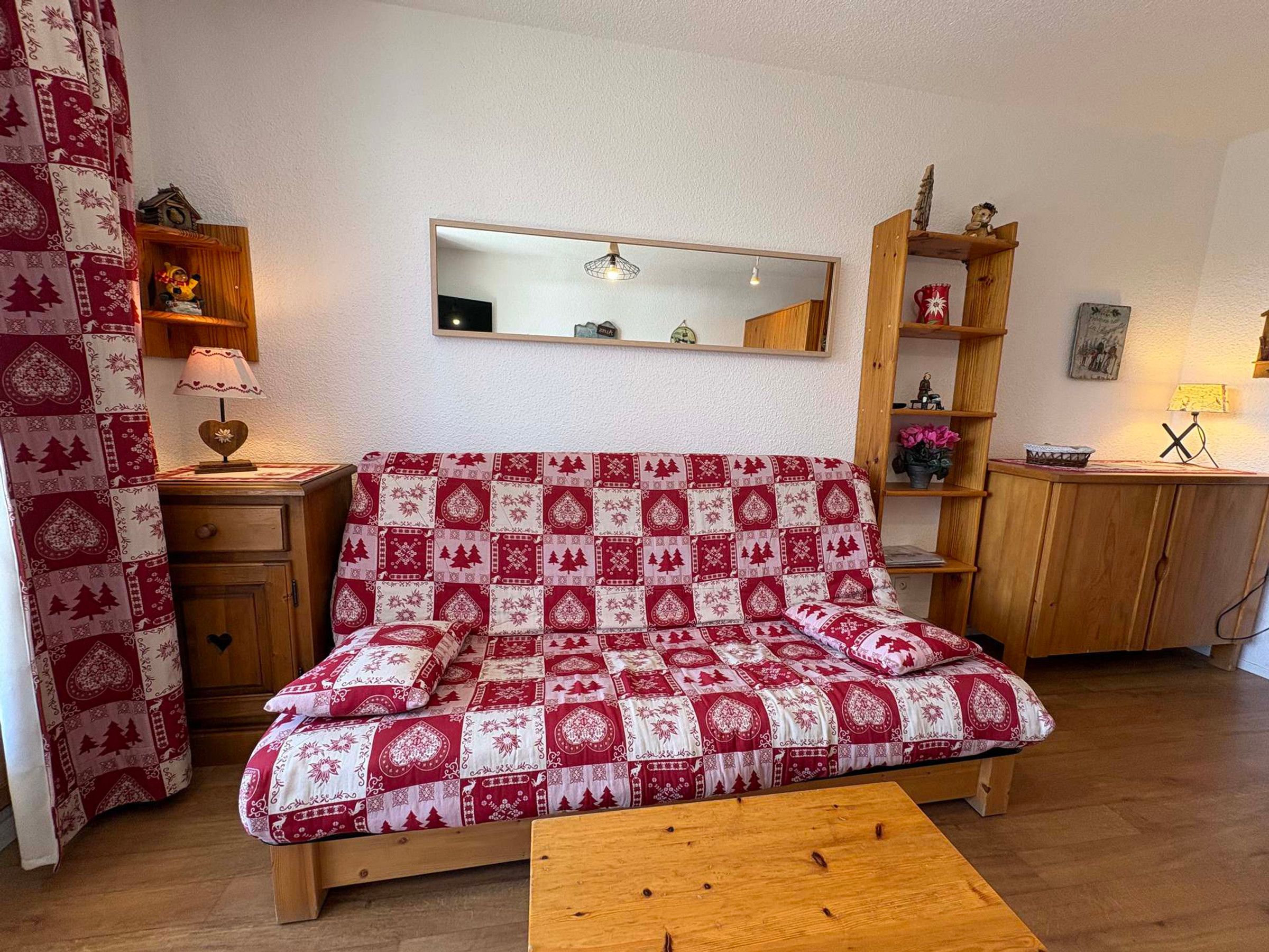 Una sala de estar acogedora con un sofá estampado, una mesa de centro de madera, un espejo y una estantería.