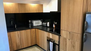 Eine moderne Küche mit Holzschränken, einer schwarzen Arbeitsplatte, einer Mikrowelle, einer Kaffeemaschine, einem Toaster und einem Edelstahlkühlschrank.