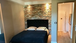 Ein Schlafzimmer mit Steinstruktur, einem schwarzen, gepolsterten Kopfteil und Holzboden.