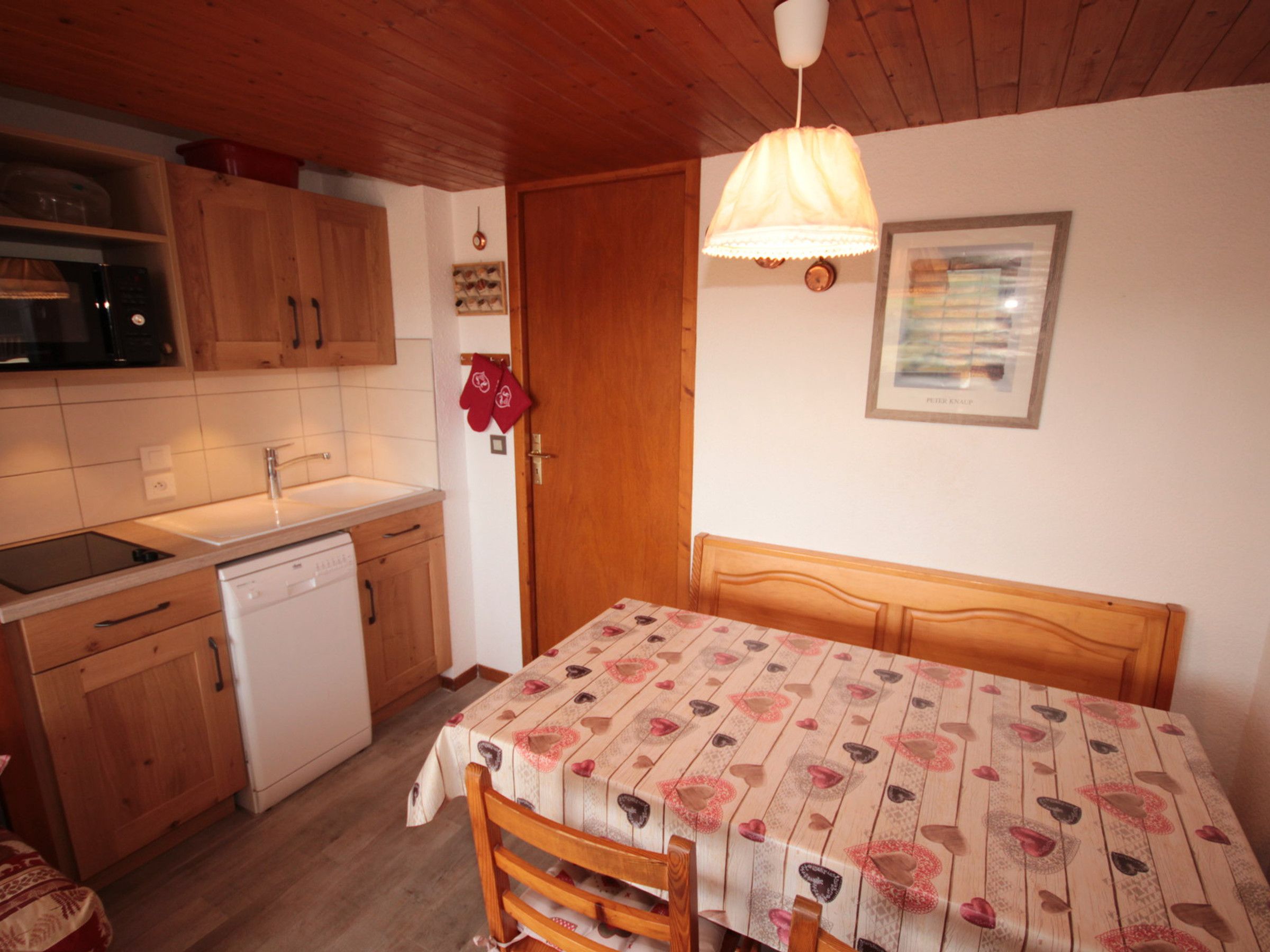 A compact kitchen with wooden cabinets, a dishwasher, and a table with a heart-patterned tablecloth.