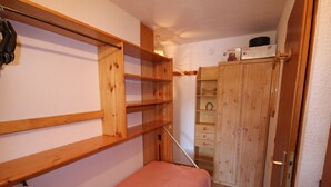 Een kleine kamer met een stapelbed, een houten garderobe en een bureau.