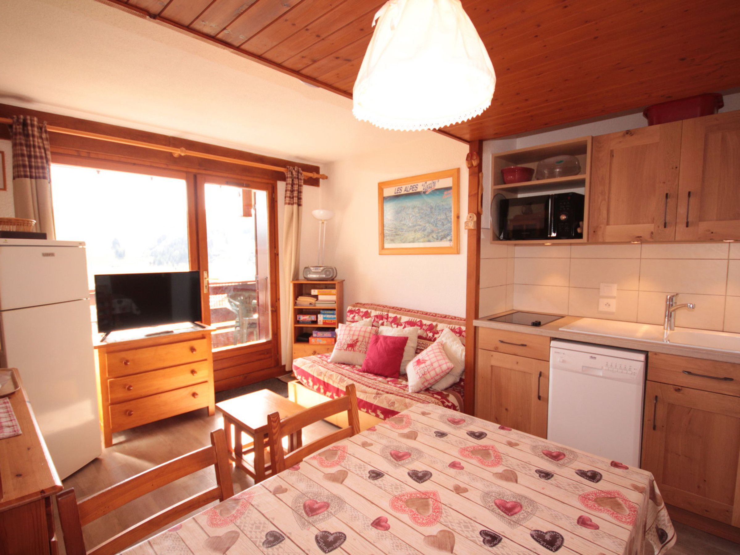 Ein gemütliches Zimmer mit Bett, Fernseher, Esstisch und Küchenzeile.