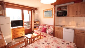 Een gezellige kamer met een bed, een televisie, een eettafel en een kitchenette.