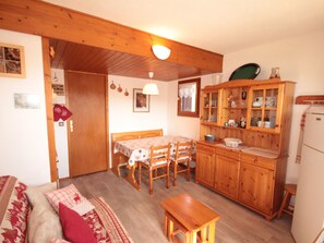 A cozy living room with a sofa, a wooden table, and a kitchen area with wooden cabinets and a refrigerator.