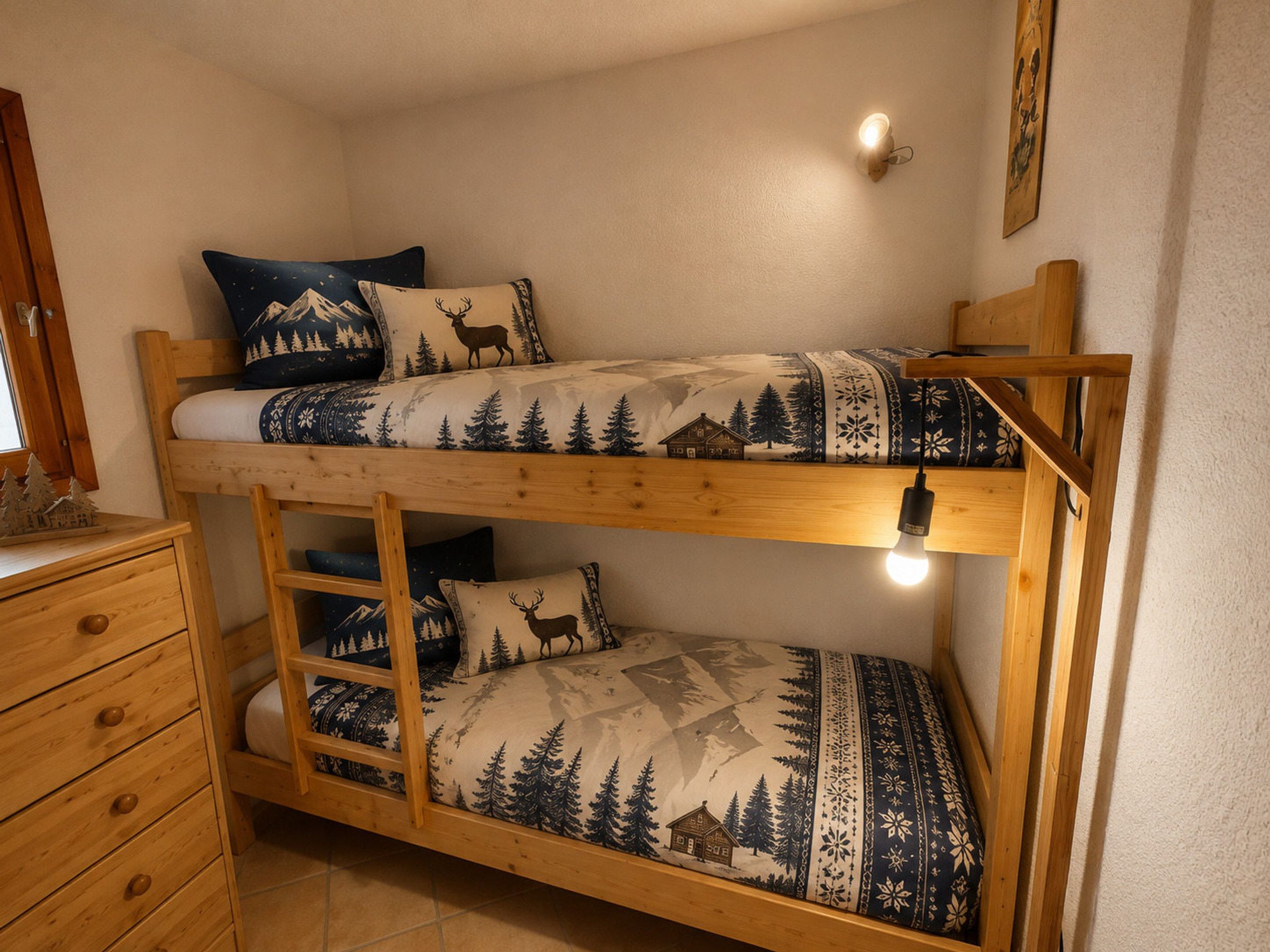 A bunk bed with a wooden frame, two pillows with animal prints, a small wooden dresser, and a wall-mounted light fixture.