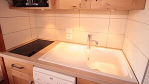 Een keuken met een zwart inductiekookplaatje, een witte spoelbak, houten keukenkastjes en een vaatwasser.