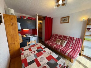 A compact living space with a kitchenette, a sofa, and a table with a quilt. - Cozy cabin studio for 4 at Les Saisies, pets allowed (Les Saisies)
