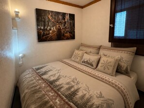 Une chambre à coucher avec un lit, un tableau représentant des cerfs accroché au mur et une fenêtre donnant sur un paysage.