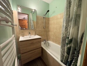 Een badkamer met een wastafel, spiegel, douche en een houten opbergmeubel.