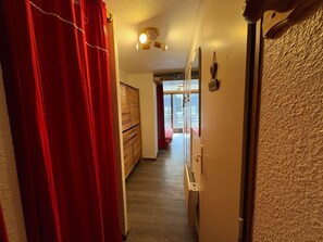 Un couloir avec une armoire en bois, un rideau rouge et une porte donnant sur une pièce où se trouve un lit.