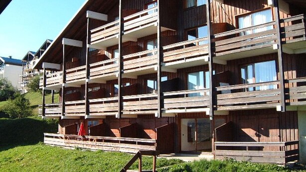 Een meerhoog gebouw van hout met balkons, een overdekte ingang en een gazon ervoor.
