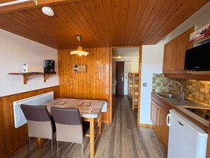 A compact kitchen with wooden cabinets, a dining area with a table and chairs, and a microwave on the countertop.