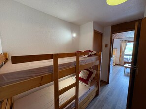 A bunk bed room with a wooden headboard, a small table, and a door leading to another room.