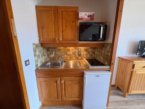 A compact kitchen with wooden cabinets, a built-in microwave, a sink, and a refrigerator.