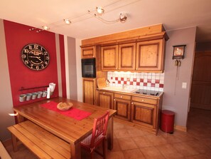A kitchen with wooden cabinets, a red wall clock, a tiled backsplash, and a wooden dining table with chairs.