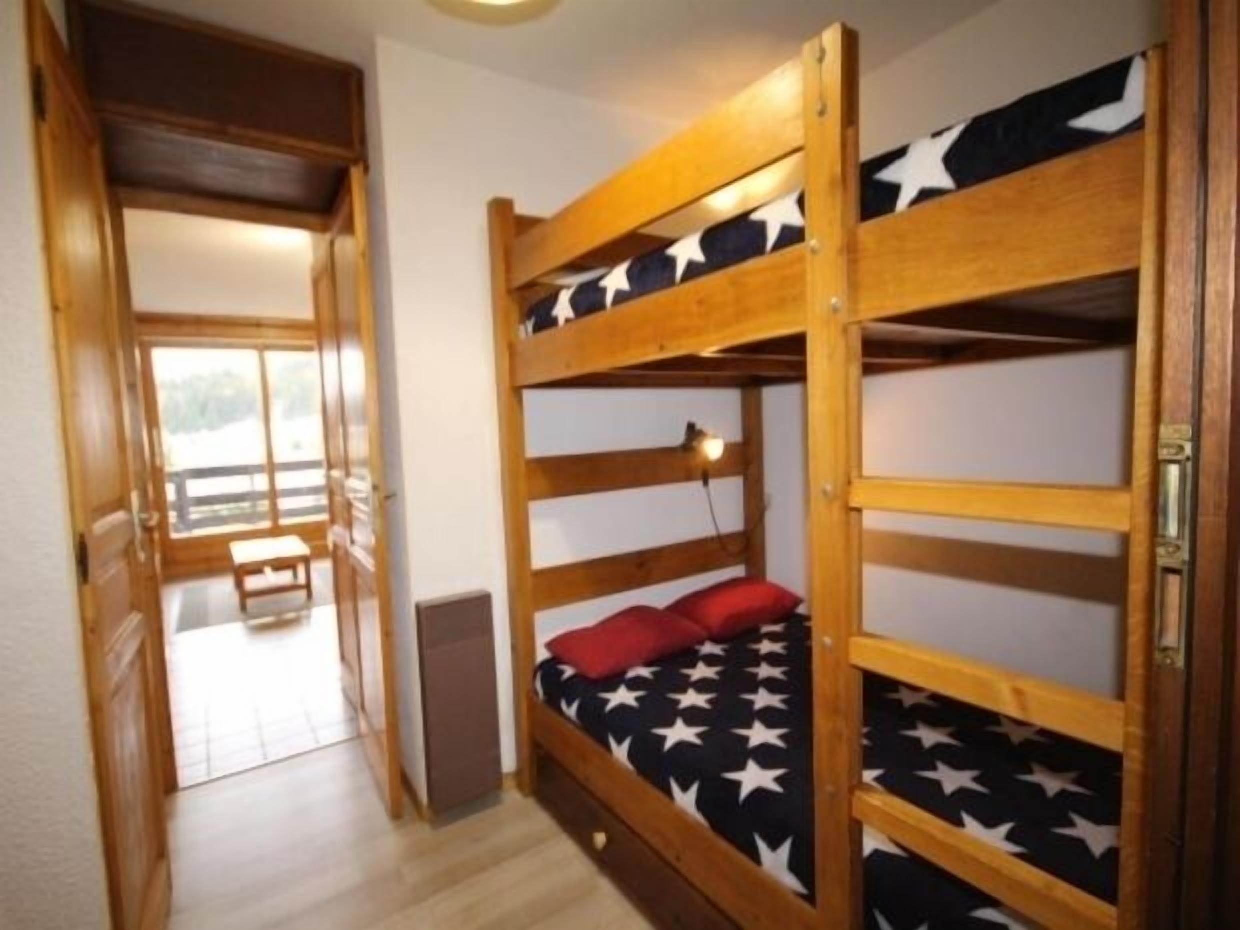 Ein Mehrbettzimmer mit einem Bettbezug mit Sternenmuster, einer kleinen Bank und einer Tür, die auf einen Balkon führt.