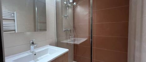 Un baño moderno con lavamanos blanco, espejo y cabina de ducha.