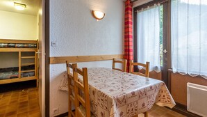 A room with a wooden table, chairs, a bunk bed, a wall-mounted light, and a window with curtains. - Central apartment, 4 pers, Parking, Wifi (La Clusaz)