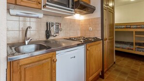 A compact kitchen with wooden cabinets, a built-in microwave, a gas stove, and a dishwasher. - Central apartment, 4 pers, Parking, Wifi (La Clusaz)