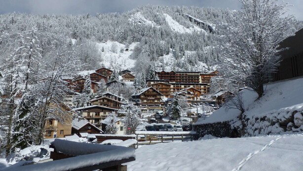 A snow-covered mountain village with wooden buildings, a ski slope, and a clear sky. - Central apartment, 4 pers, Parking, Wifi (La Clusaz)