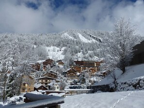 A snow-covered mountain village with wooden buildings, a ski slope, and a clear sky.