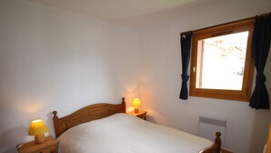 A bedroom with a wooden bed, two bedside lamps, a window with curtains, and a radiator.
