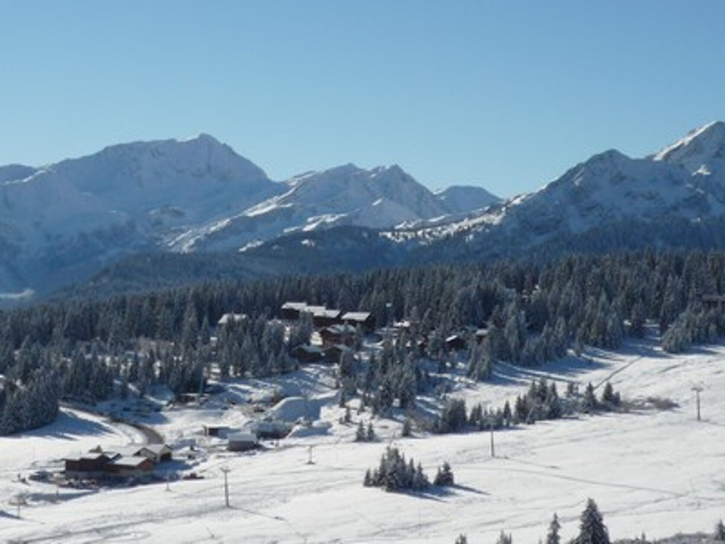 A snow-covered mountain landscape with a ski resort, including buildings and ski lifts.
