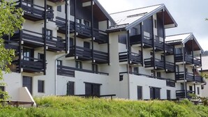 A modern multi-story residential building with balconies, white walls, and dark railings.