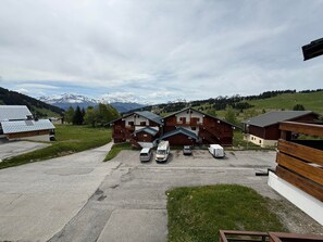 Un bâtiment situé en zone rurale, doté d’un espace de stationnement et entouré de champs verdoyants, avec des montagnes en arrière-plan.