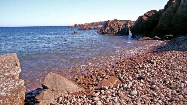 A rocky beach with clear water and large boulders.
