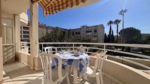 A balcony with a table and chairs, a striped awning, and a view of apartment buildings.