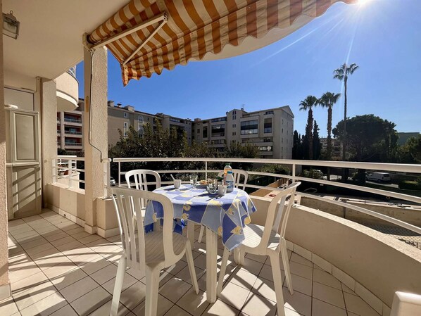 Uma varanda com mesa e cadeiras, um toldo listrado e vista para prédios de apartamentos.